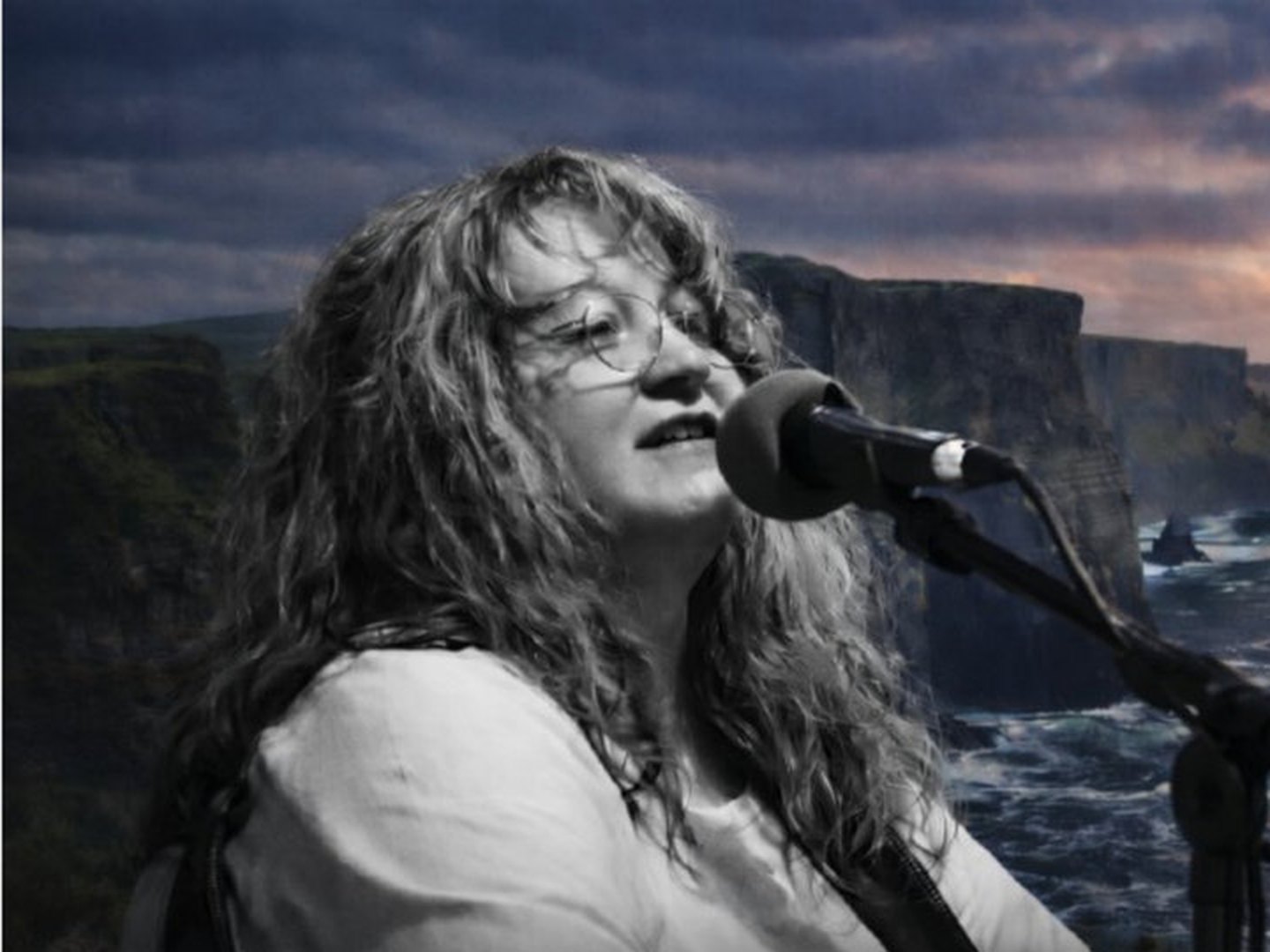 Jane Maria Williams singing into a microphone with sea cliffs behind her