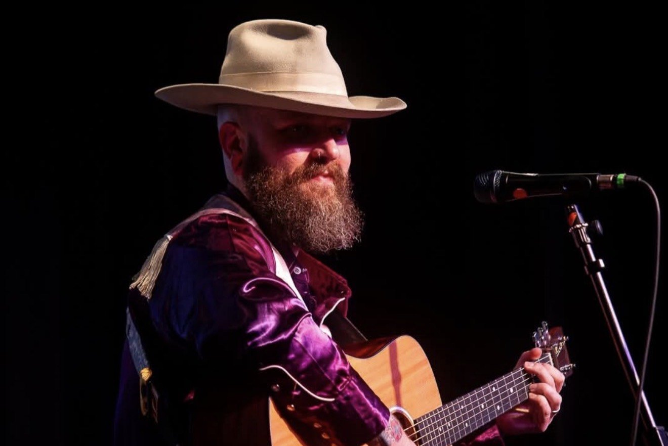 Rory E. Lee on stage in a stetson and western shirt, playing acoustic guitar