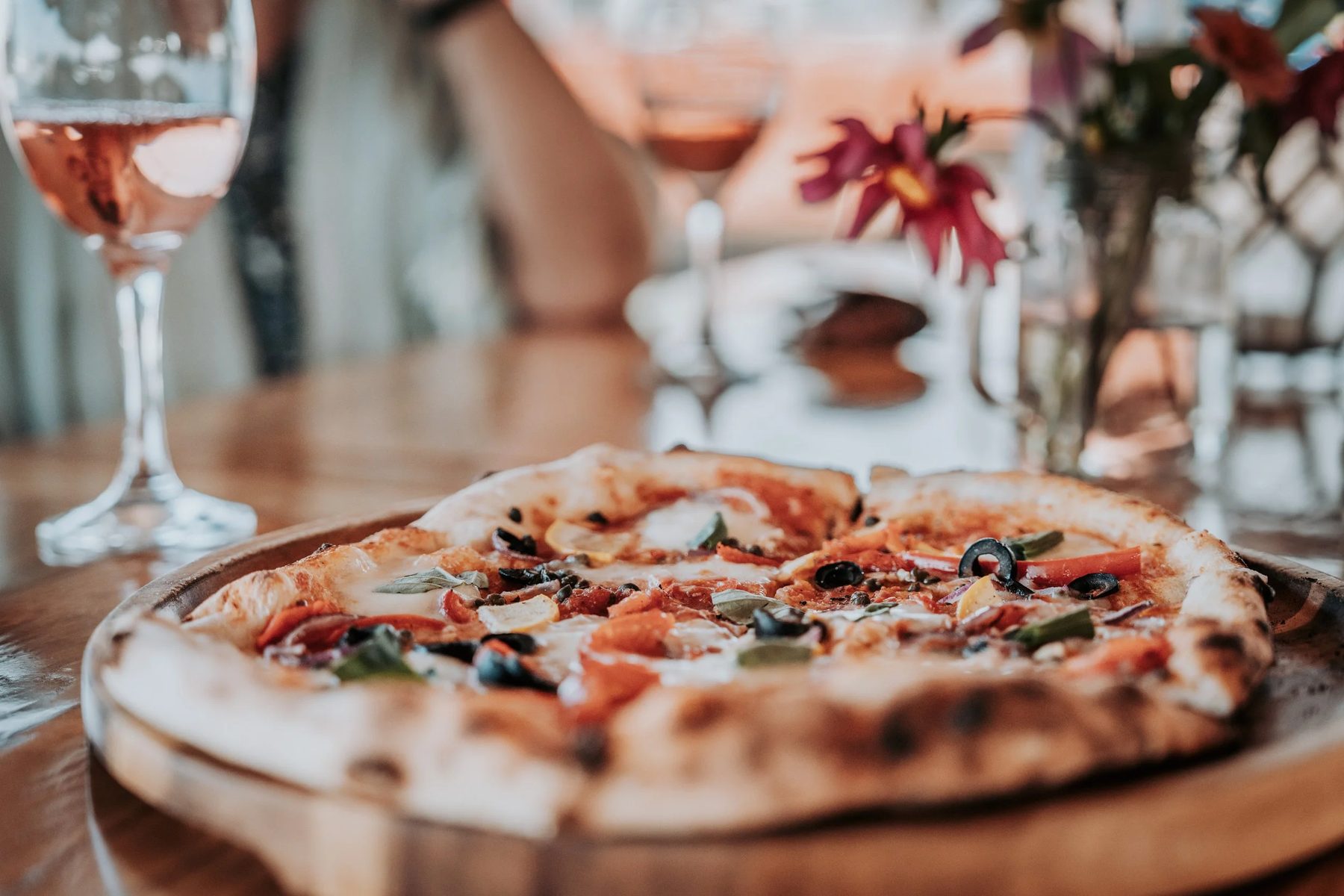 A freshly baked pizza on a wooden table with a glass of rosé